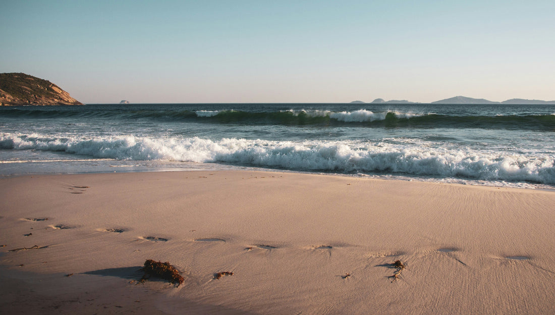 Footprints left in the sand by the edge of the ocean. Mountainous islands are in the background