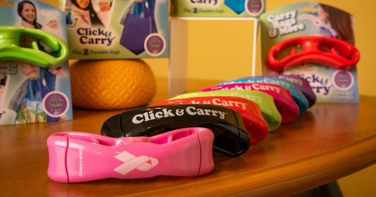 Many colors of Click & Carry grocery carrying handles lined up on a table with some displayed in packaging in the background