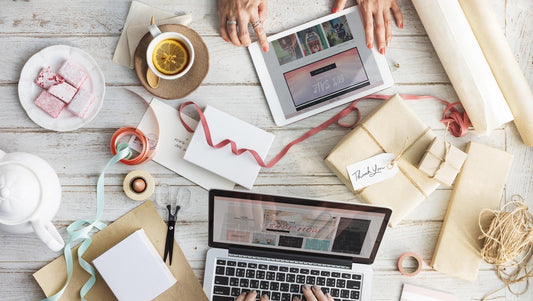 Overhead view of a laptop and tablet being used on a wooden surface surrounded by miscellaneous crafting supplies