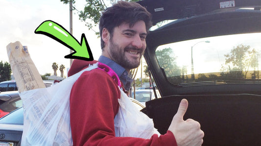 Man using a fuchsia Click & Carry grocery handle to haul two bags over his shoulder outside in front of an open car trunk