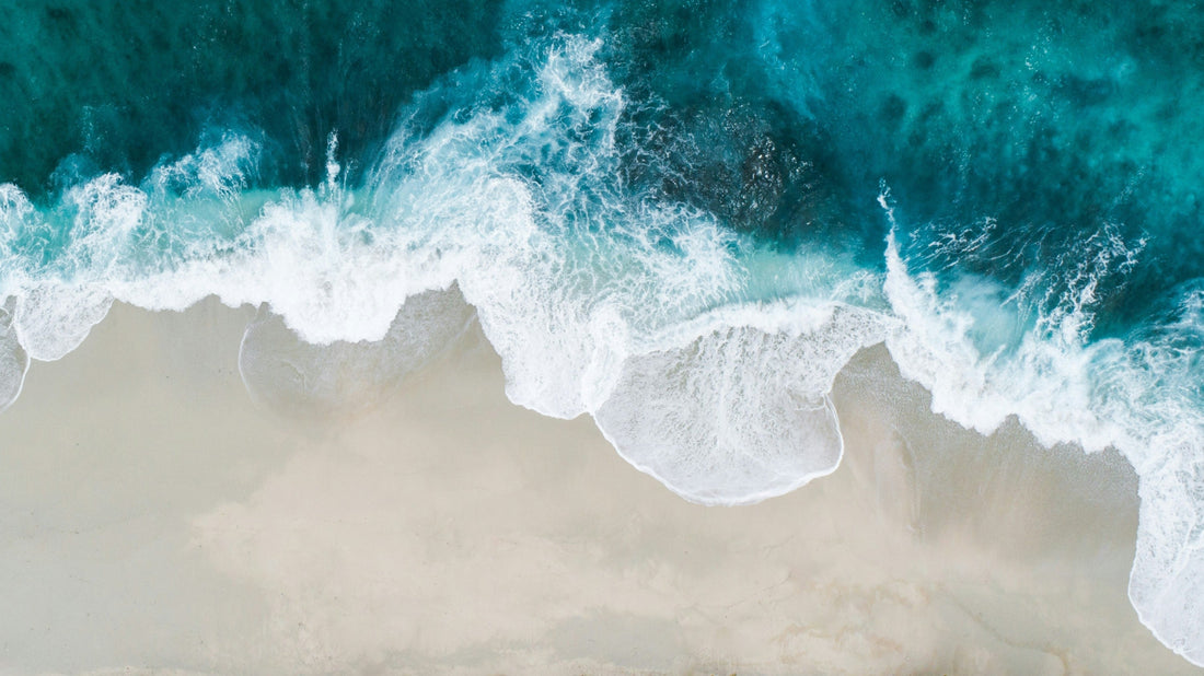 Overhead view of a blue wave crashing on a sandy beach