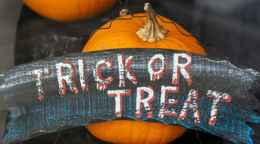 Orange pumpkin with a weathered "trick or treat" sign hanging from it by a wire in a dark setting